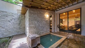 A stone-walled pool area with a wooden deck, stone flooring, and wicker chairs. - Mori No Izumi (Ito)