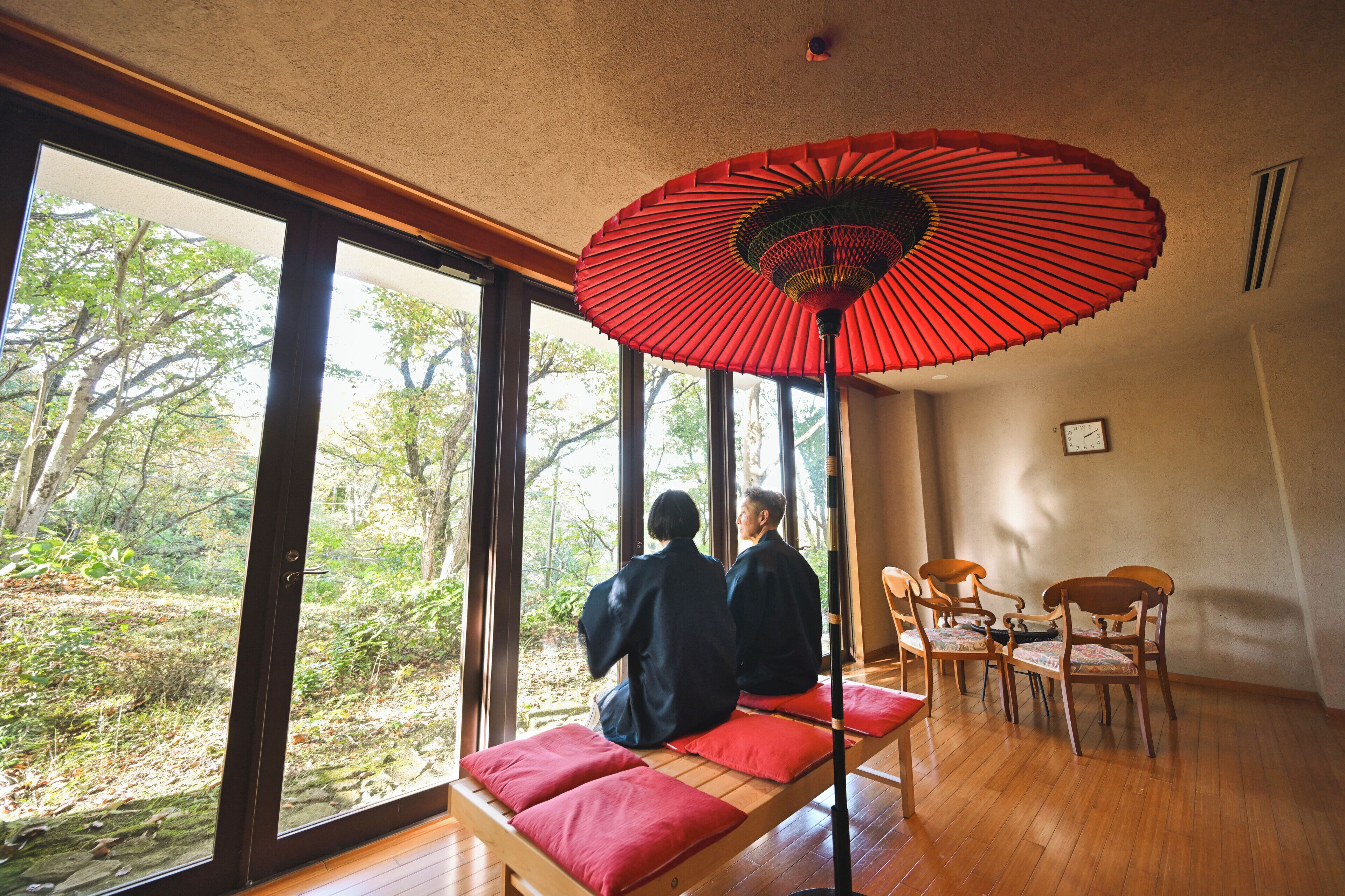 A room with large windows, a red fan, and a wooden floor.