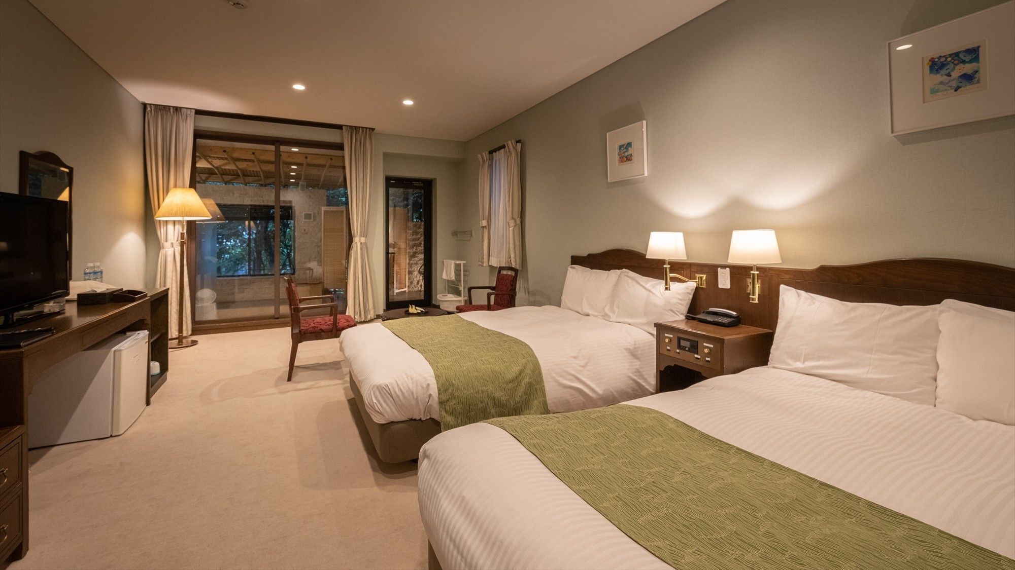 A hotel room with two beds, a desk with a TV, a chair, a nightstand with lamps, and a window with curtains.