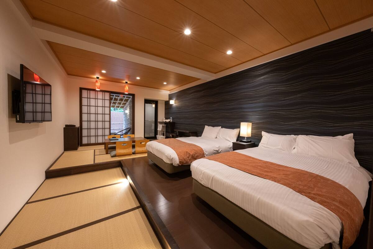 A hotel room with two beds, tatami mats, a wooden ceiling, and a dark textured wall.
