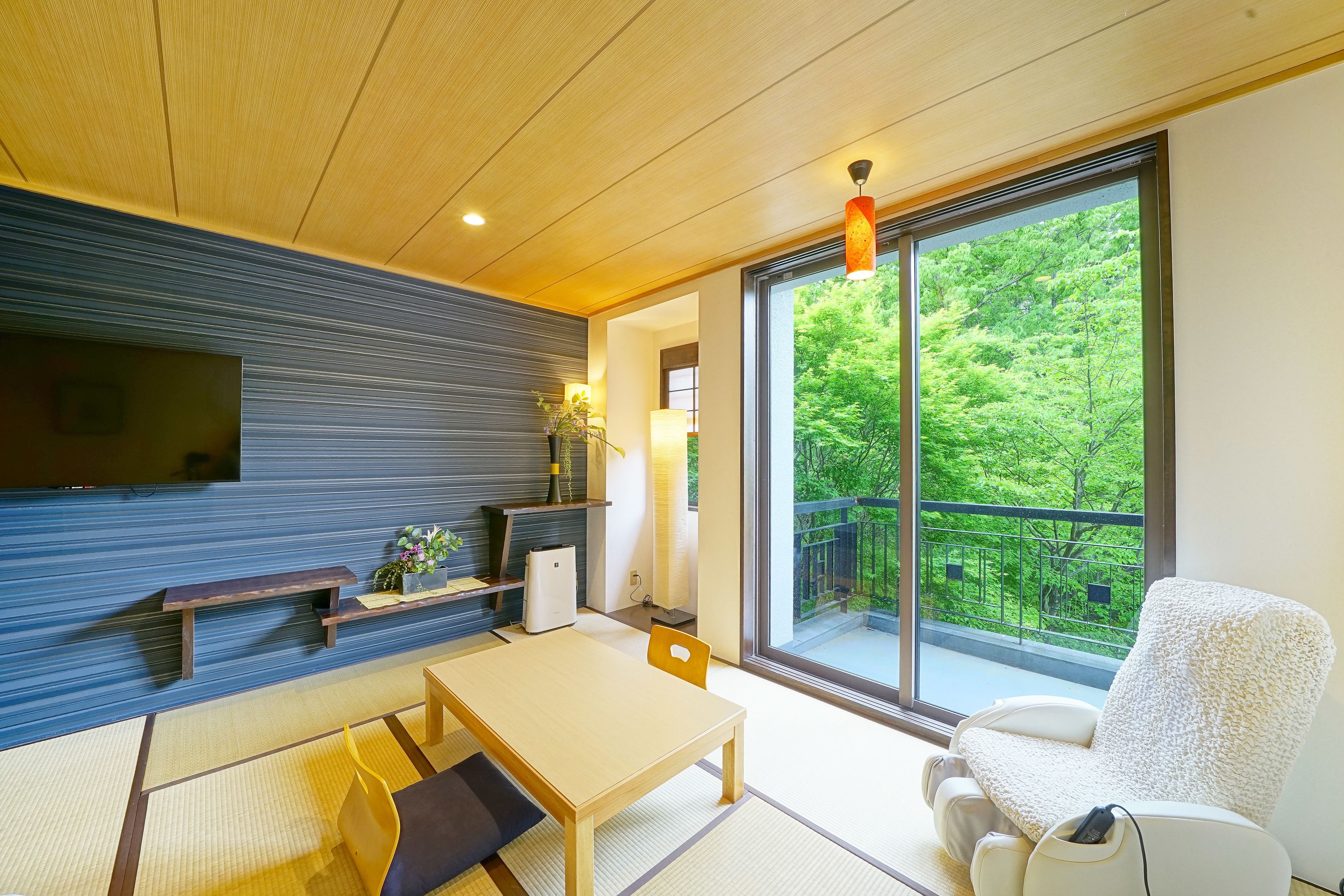 A modern living room with a wooden ceiling, a large window with a view of greenery, a sofa, a table, and a TV mounted on the wall.