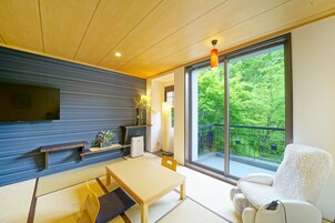 A modern living room with a wooden ceiling, a large window with a view of greenery, a sofa, a table, and a TV mounted on the wall.