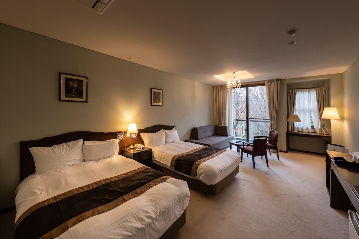A hotel room with two beds, a sofa, a desk, and a chair.