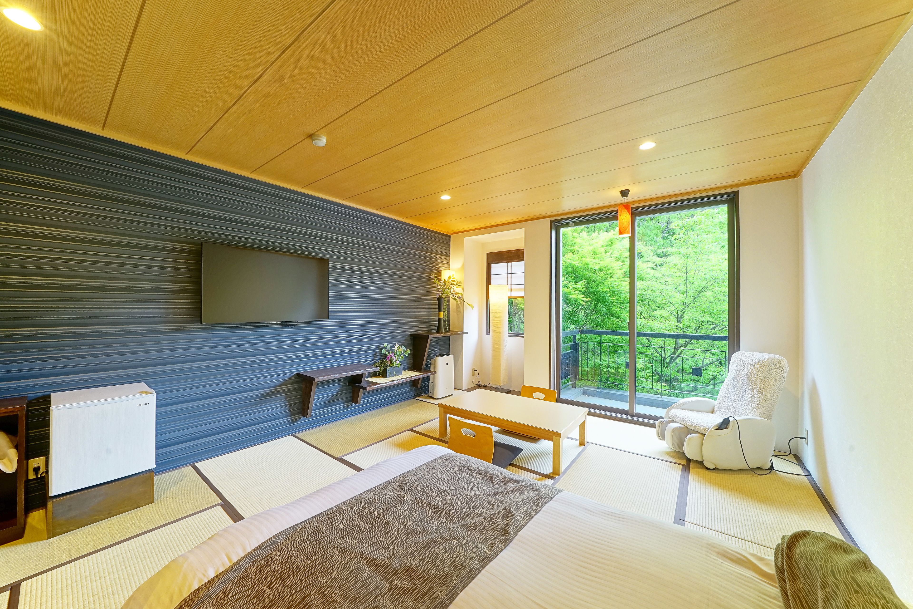 Habitació moderna amb paviment de tatami, televisió de pantalla plana penjada a la paret, taula de fusta i una finestra gran amb vista a la vegetació.