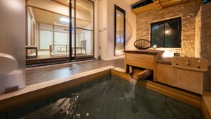 A traditional Japanese onsen with a wooden bench, a stone wall, and a window overlooking a room with tatami mats. - Mori No Izumi (Ito)