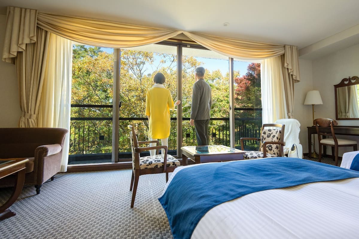 Ein Hotelzimmer mit großem Fenster, einem Bett, einem Schreibtisch, einem Sessel und einer Couch.