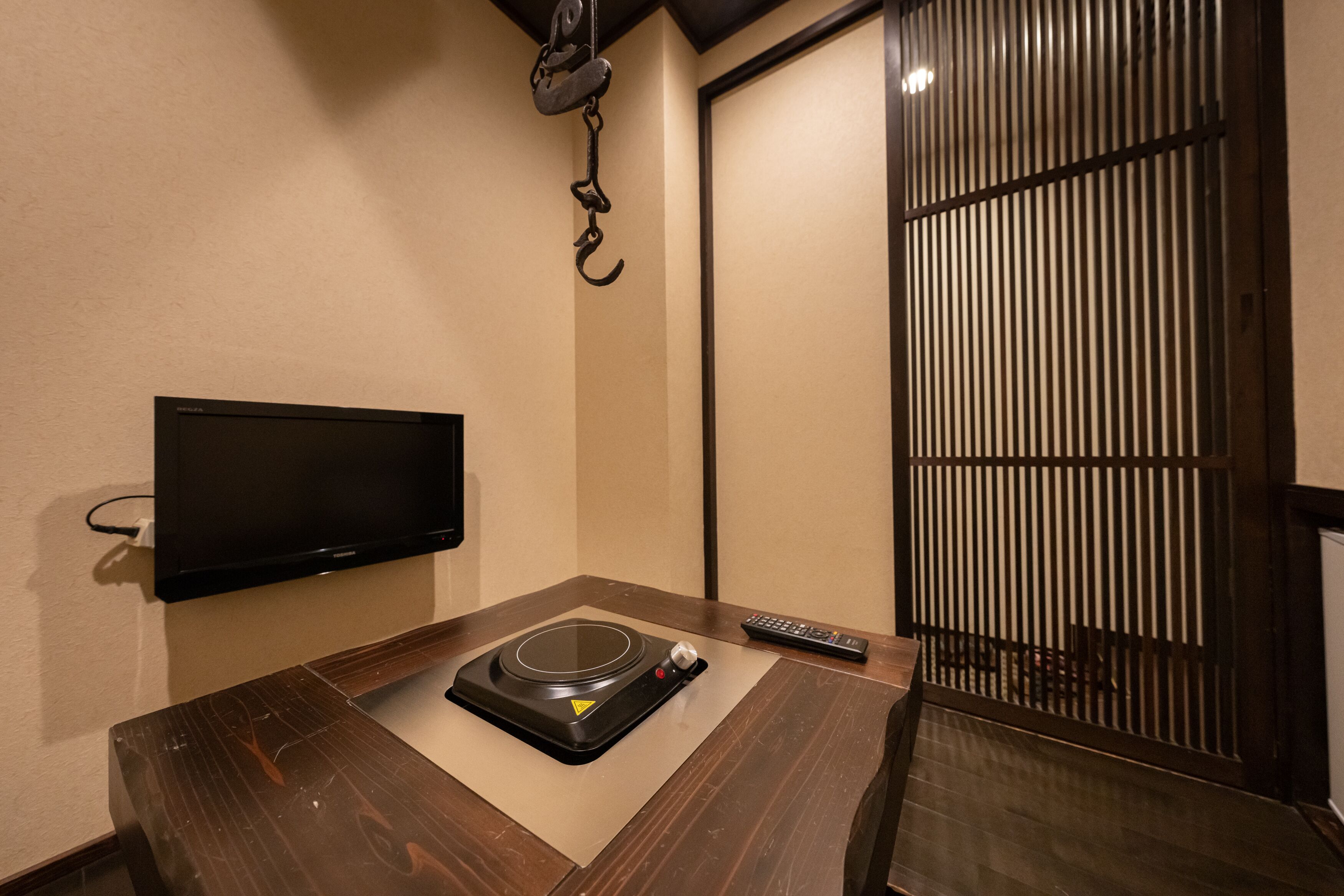 Una habitación con una televisión de pantalla plana montada en la pared, una mesa de madera con un tocadiscos, un control remoto y una puerta corredera con persianas verticales.