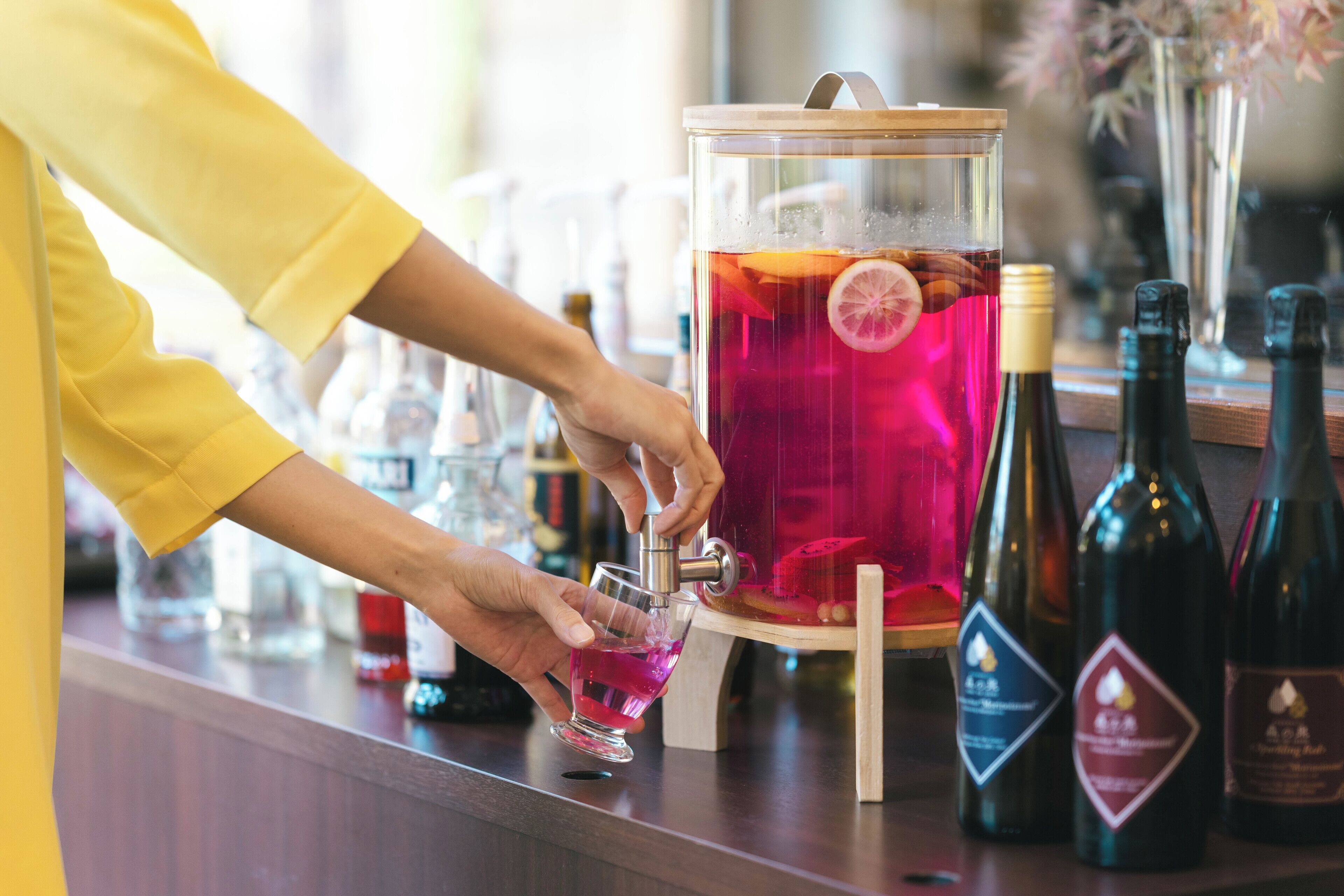 Une personne verse une boisson d’une carafe dans un verre. On peut voir des bouteilles de vin sur le comptoir.