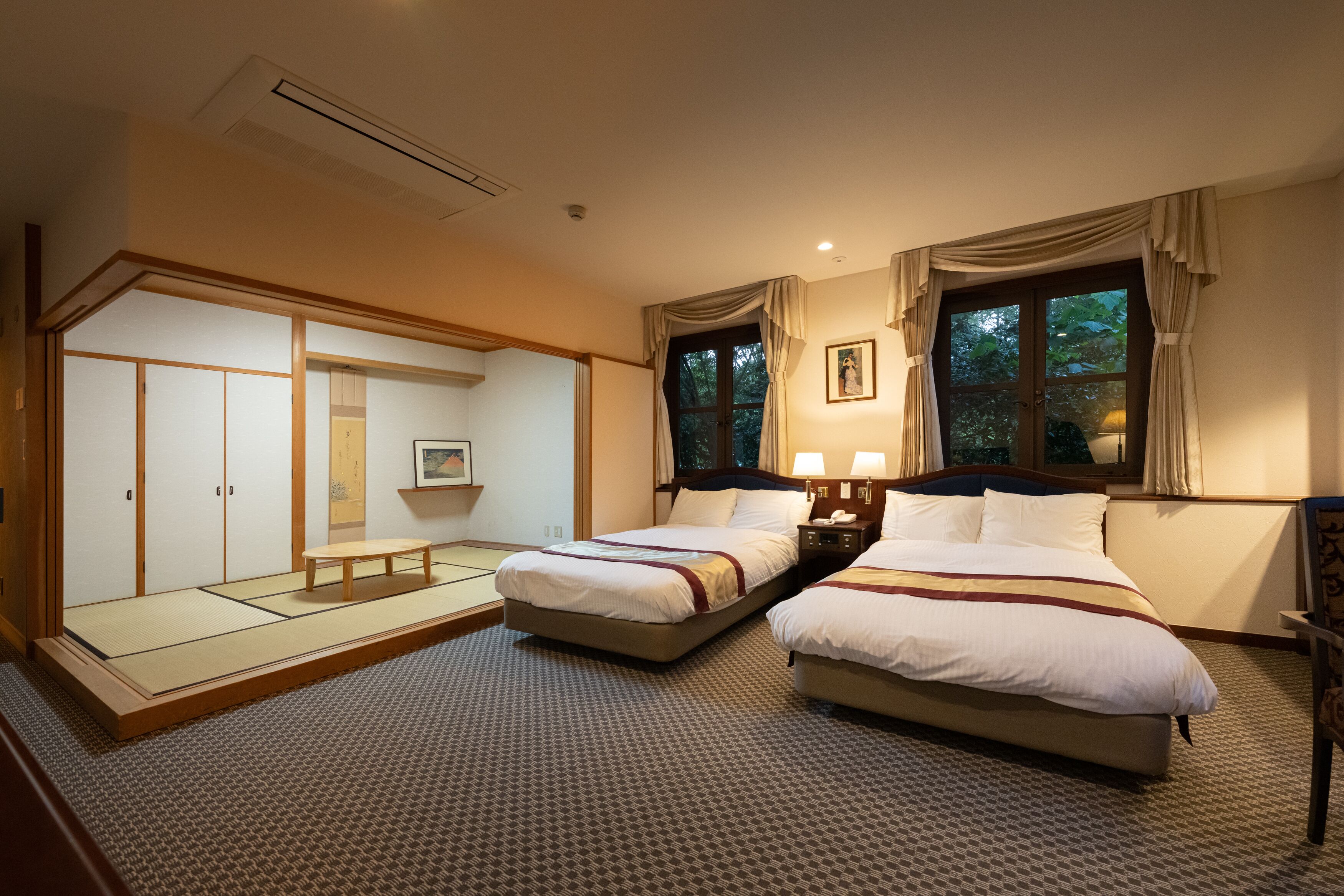 A hotel room with two beds, a tatami mat floor, a sliding door closet, and a view of trees through the window.