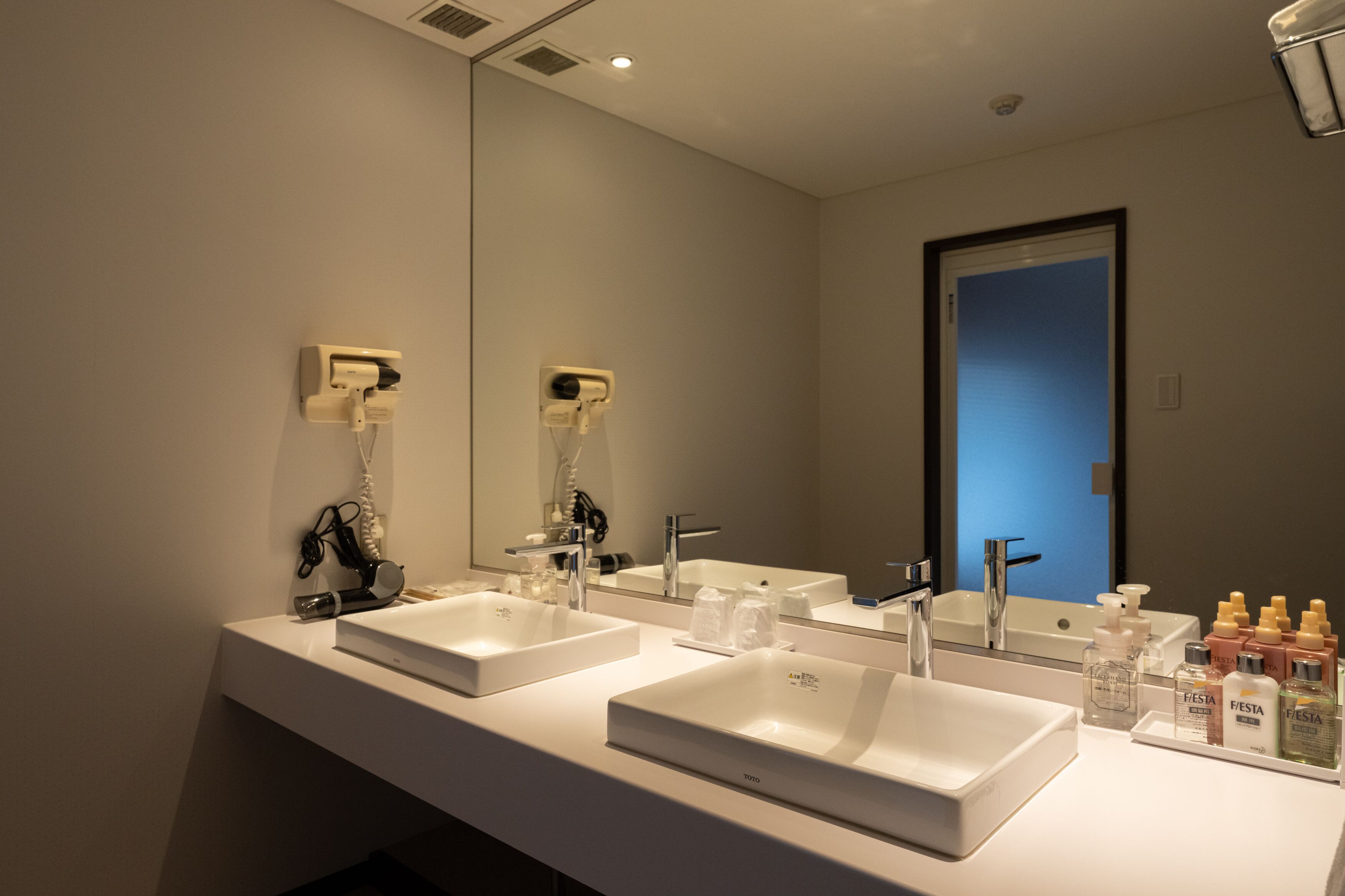 Un baño moderno con dos lavamanos, un espejo grande y una puerta que da a otra habitación.