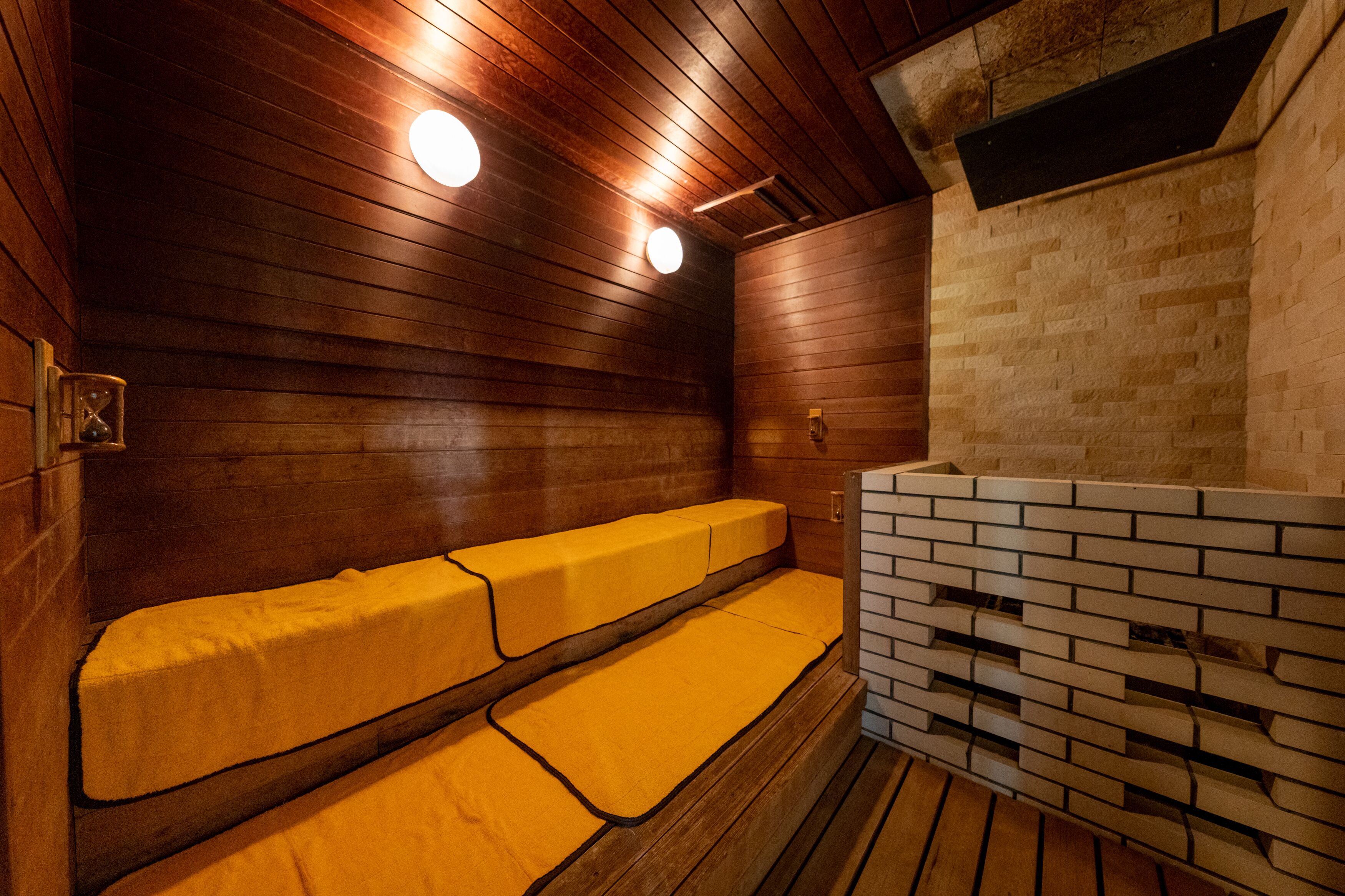 A sauna with wooden walls and benches, a brick wall, and a wooden ceiling.