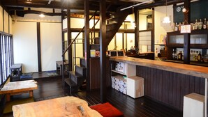 A bar area with wooden beams, a counter with bottles, and a staircase. - Guesthouse Nin-jin - Hostel (Niigata)
