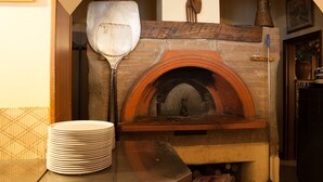 Un horno de ladrillo con un rascador metálico y una pila de platos blancos sobre una mesa.