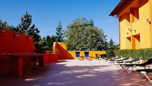 Un patio con tumbonas, piscina y un edificio de fachada amarilla.