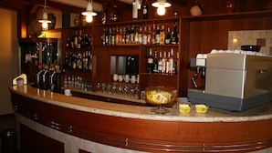 Una zona de bar con una barra curva, estantes llenos de botellas de licor, vasos y un refrigerador.
