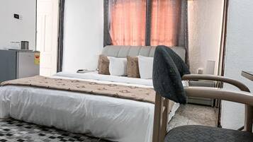 A bedroom with a bed, a chair, a desk, and a window with curtains.
