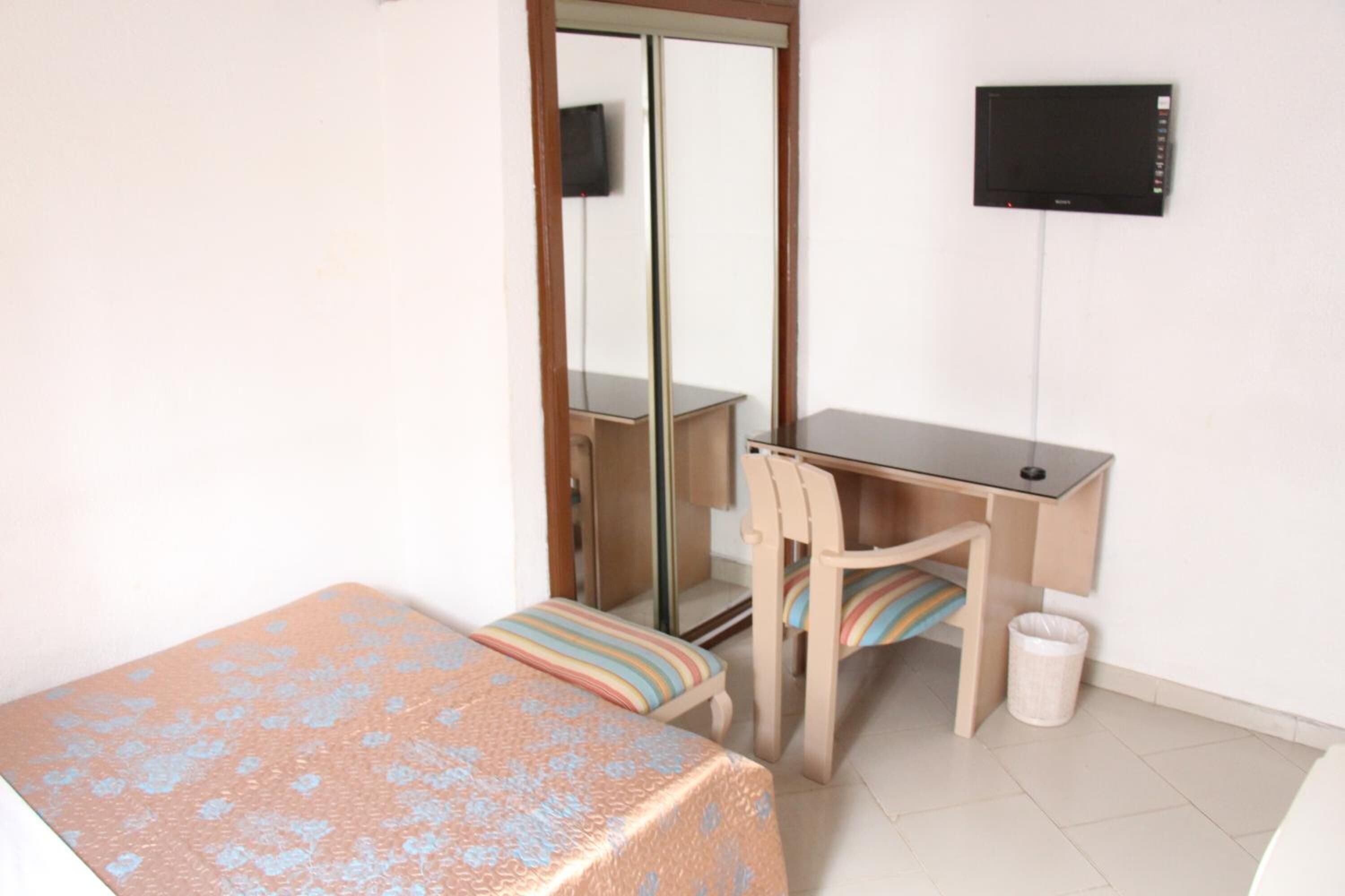Une chambre à coucher comprenant un lit, un bureau, une chaise, une télévision et une armoire.