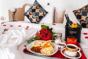 A neatly made bed with a red and white checkered bedspread, a bottle of Cristal champagne, a glass of orange juice, a plate with scrambled eggs, toast, and a small bouquet of red flowers.
