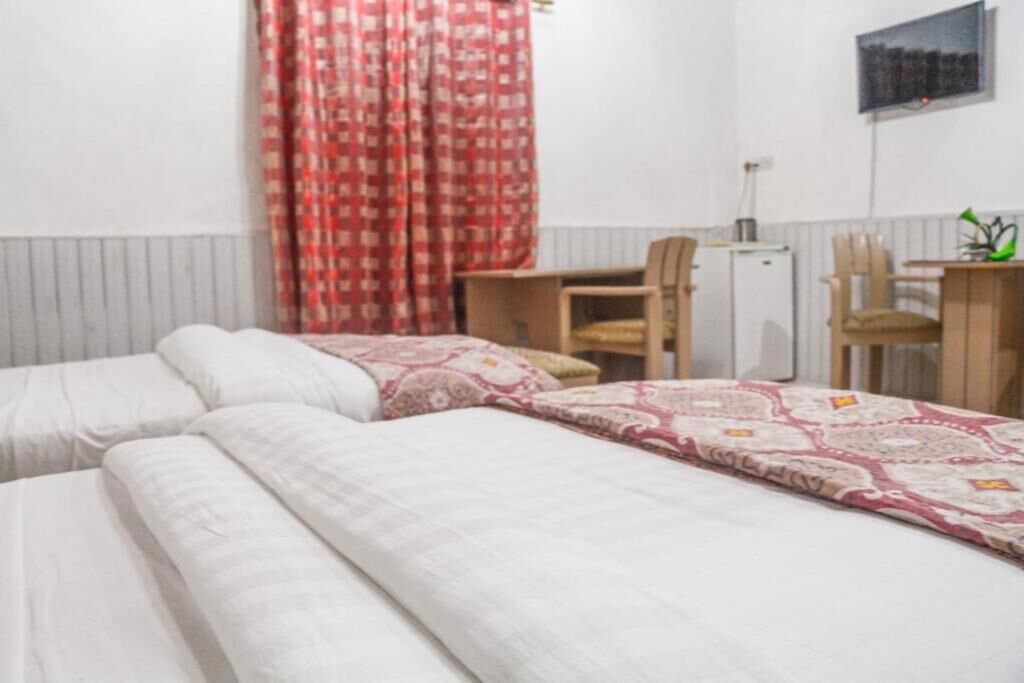 A room with two beds, a desk, a chair, and a small refrigerator.