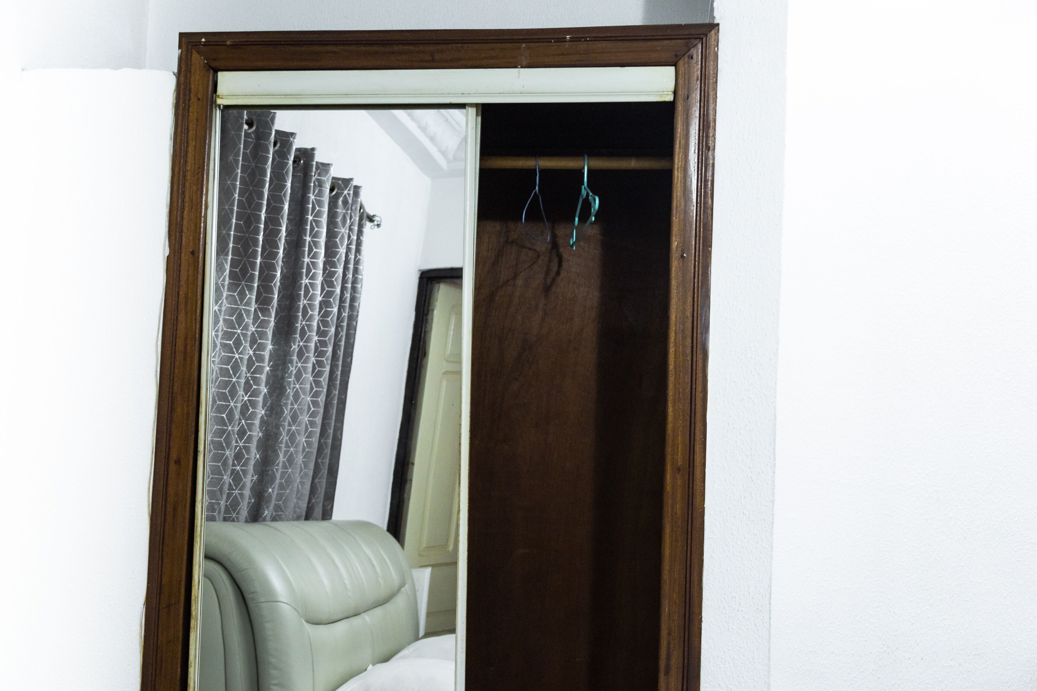 Ein Zimmer mit einem spiegelnden Holzelement, einem grünen Ledersessel, einem gemusterten Vorhang und einer Holztür.