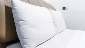 Uma cama com roupa de cama branca e cabeceira bege.