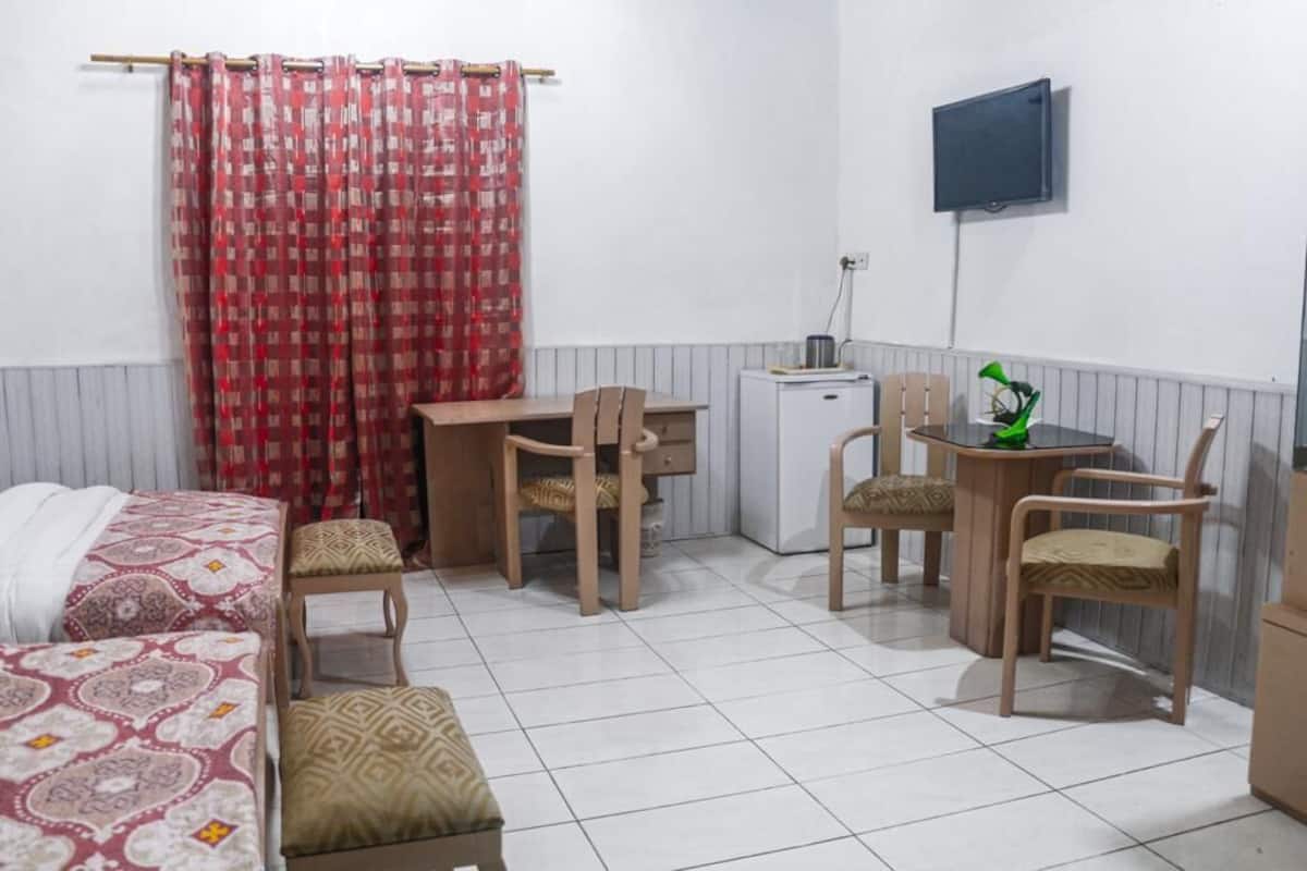 A small, clean room with a bed, a desk, two chairs, a television, and a small cabinet.