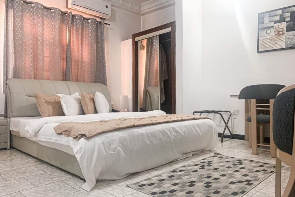 A bedroom with a bed, a bedside table, a chair, a patterned rug, and a wardrobe.