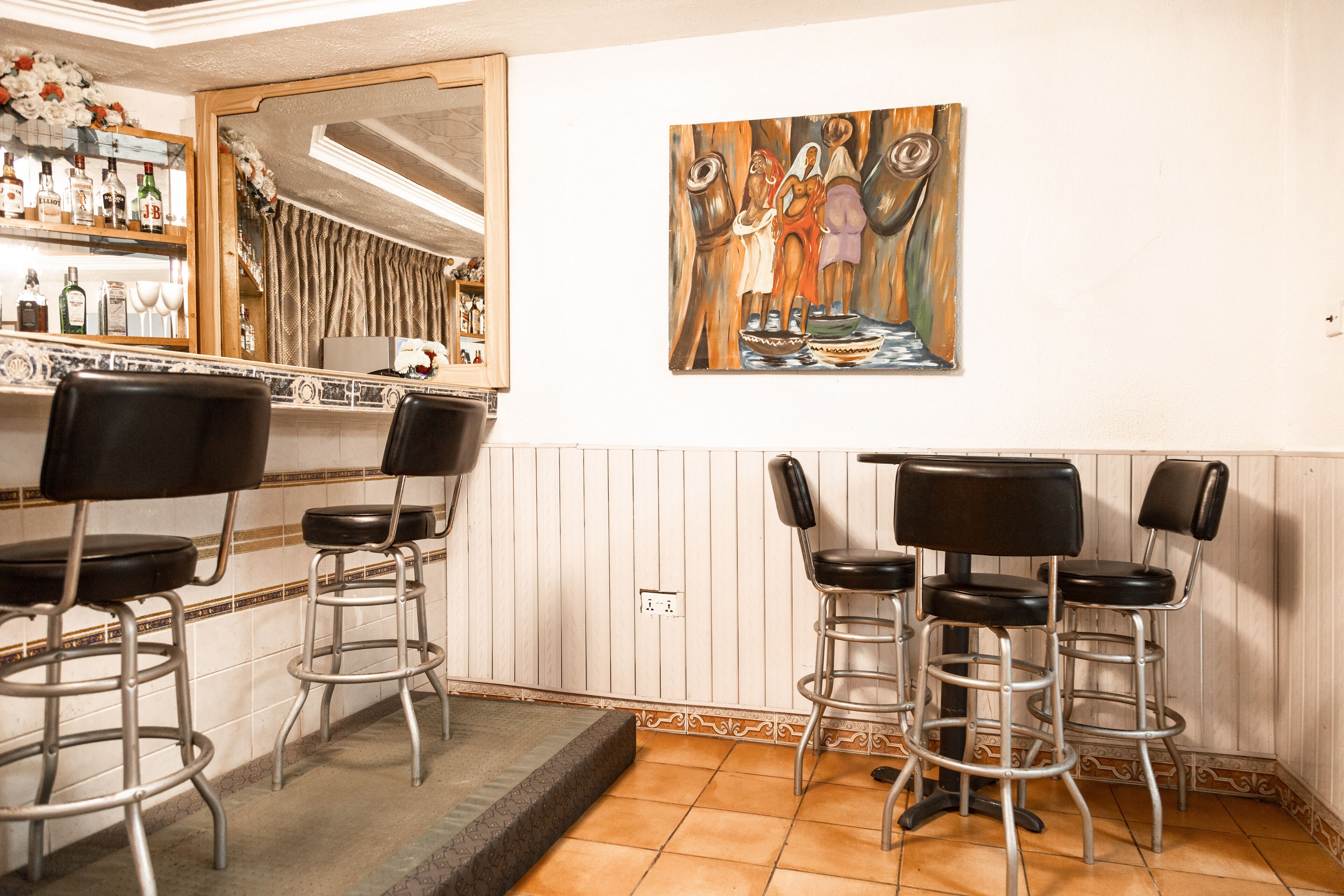 A bar area with four stools, a mirror, and a painting on the wall.