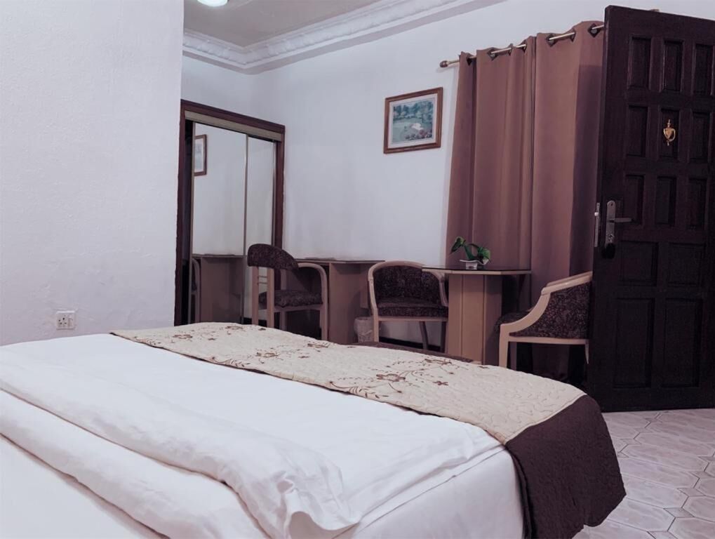 Een slaapkamer met een bed, een bureau, twee stoelen, een spiegel, een deur en een lijst met een afbeelding aan de muur.