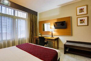 Una camera d'albergo con un letto, una scrivania, una sedia, una televisione e una panca.