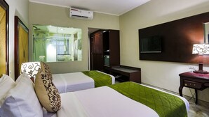 A hotel room with two beds, a desk, a mirror, and an air conditioning unit.
