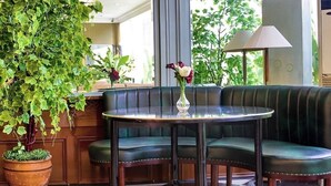 A green cushioned seating area with a glass table, a potted plant, and a vase with flowers.