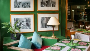 A green-themed room with framed cityscape photographs, a sofa with blue cushions, and a table with a floral table runner.