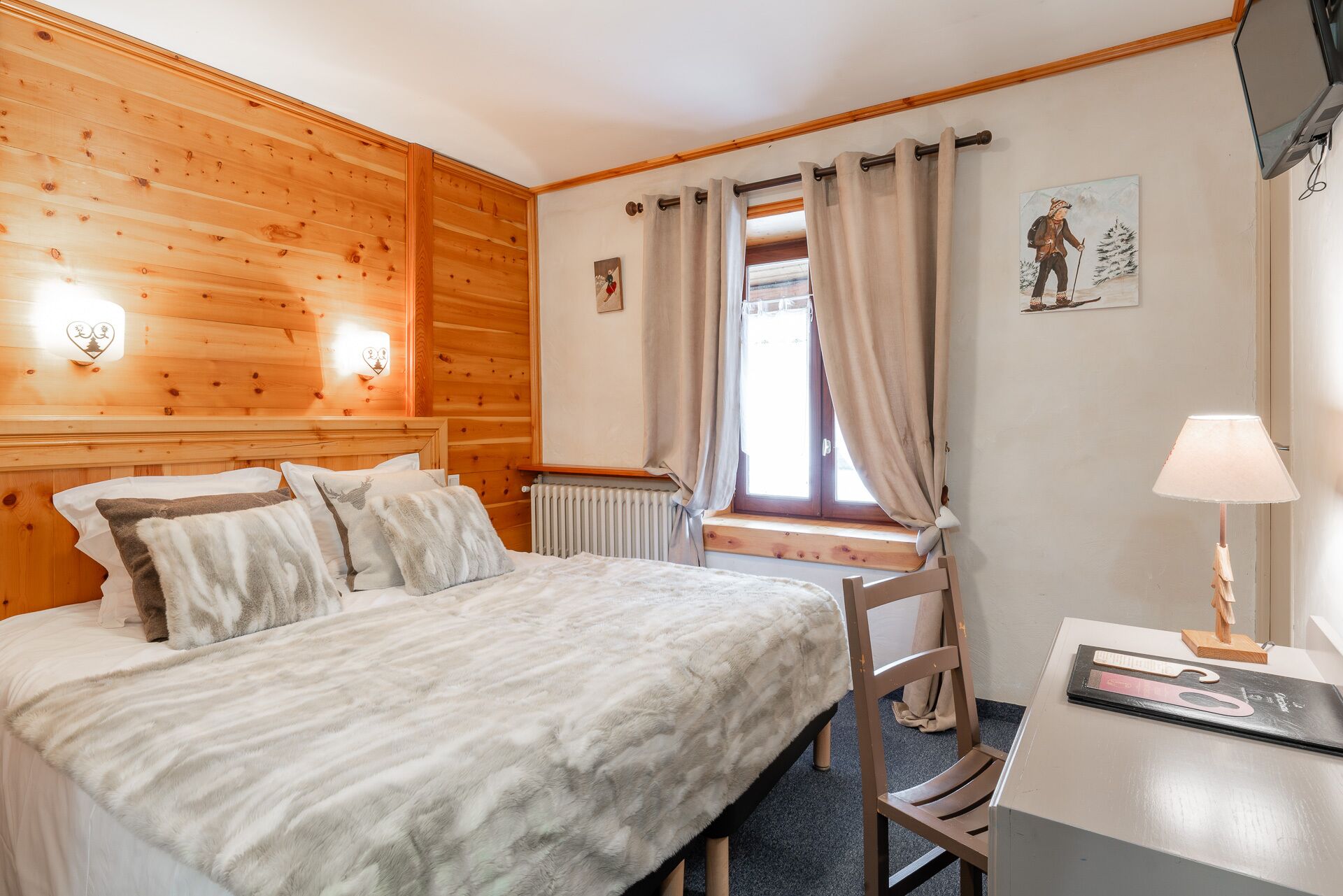 Una habitación con paneles de madera, una cama, un escritorio, una silla, un radiador y una ventana con cortinas.