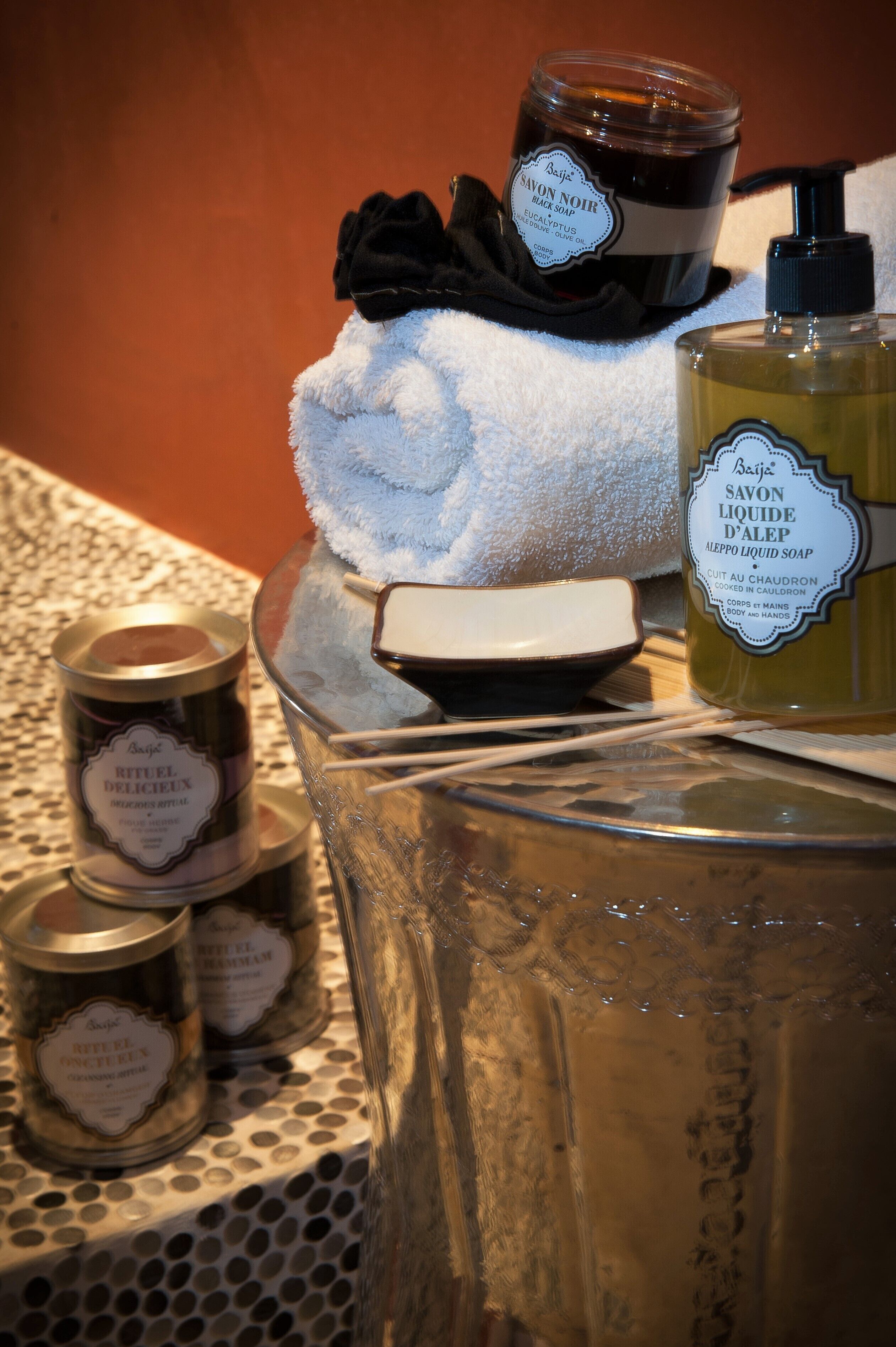 On trouvera une variété de produits de toilette, notamment un savon noir en pain, un flacon de savon liquide et plusieurs petits pots de crème ou de lotion.