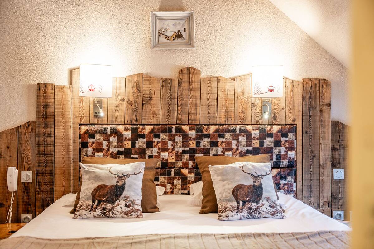 A bedroom with a wooden headboard, two pillows with deer images, a bedside phone, and a framed picture on the wall.