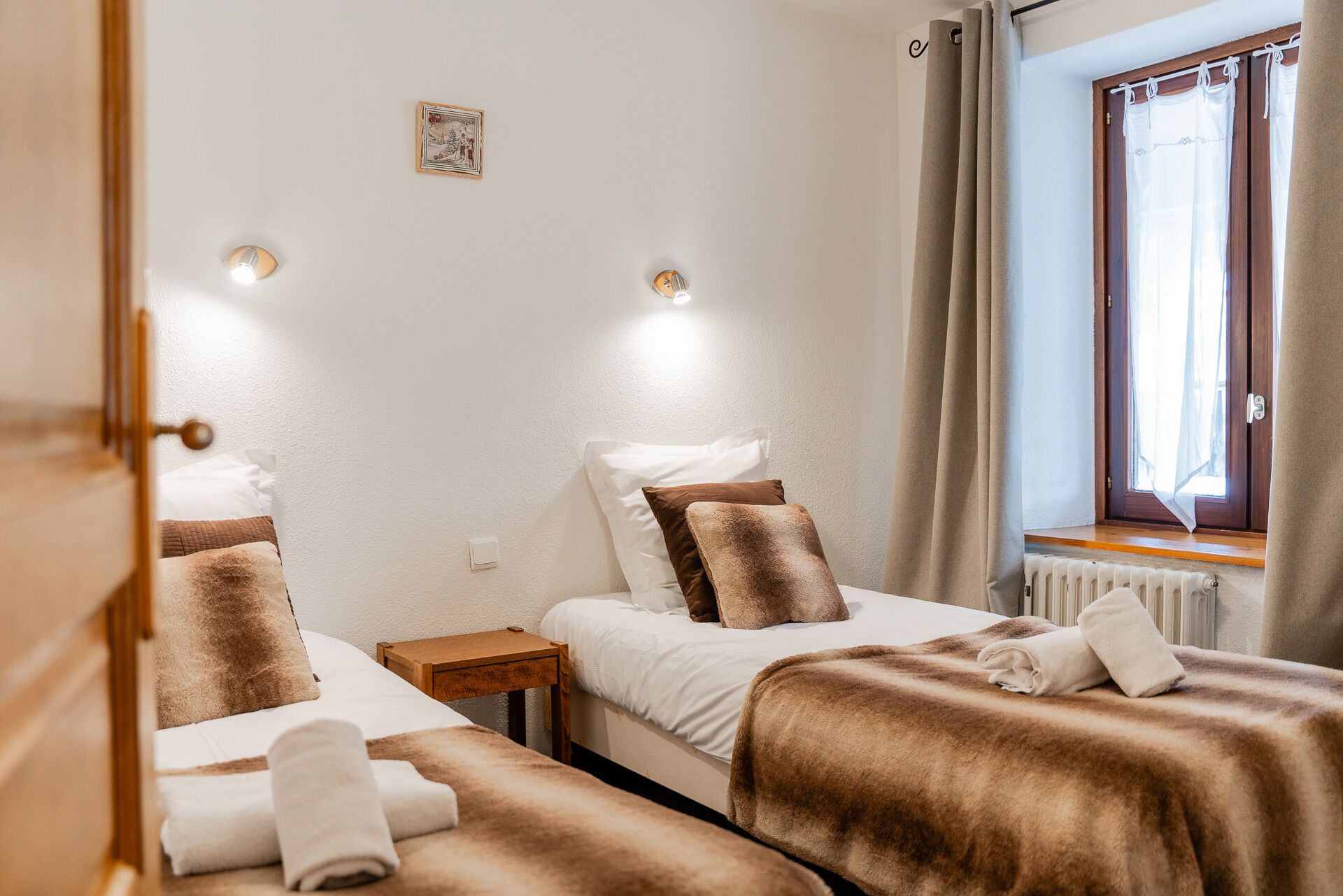 Ein Hotelzimmer mit zwei Betten, einem Fenster mit Vorhängen, einem kleinen Nachttisch und einer Wandleuchte.