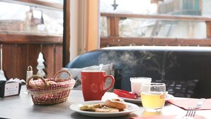 A table with a red mug, a glass of tea, a basket, and a plate with pastries. - Logis Hôtel et Spa Le Christiania (La Salle-les-Alpes)