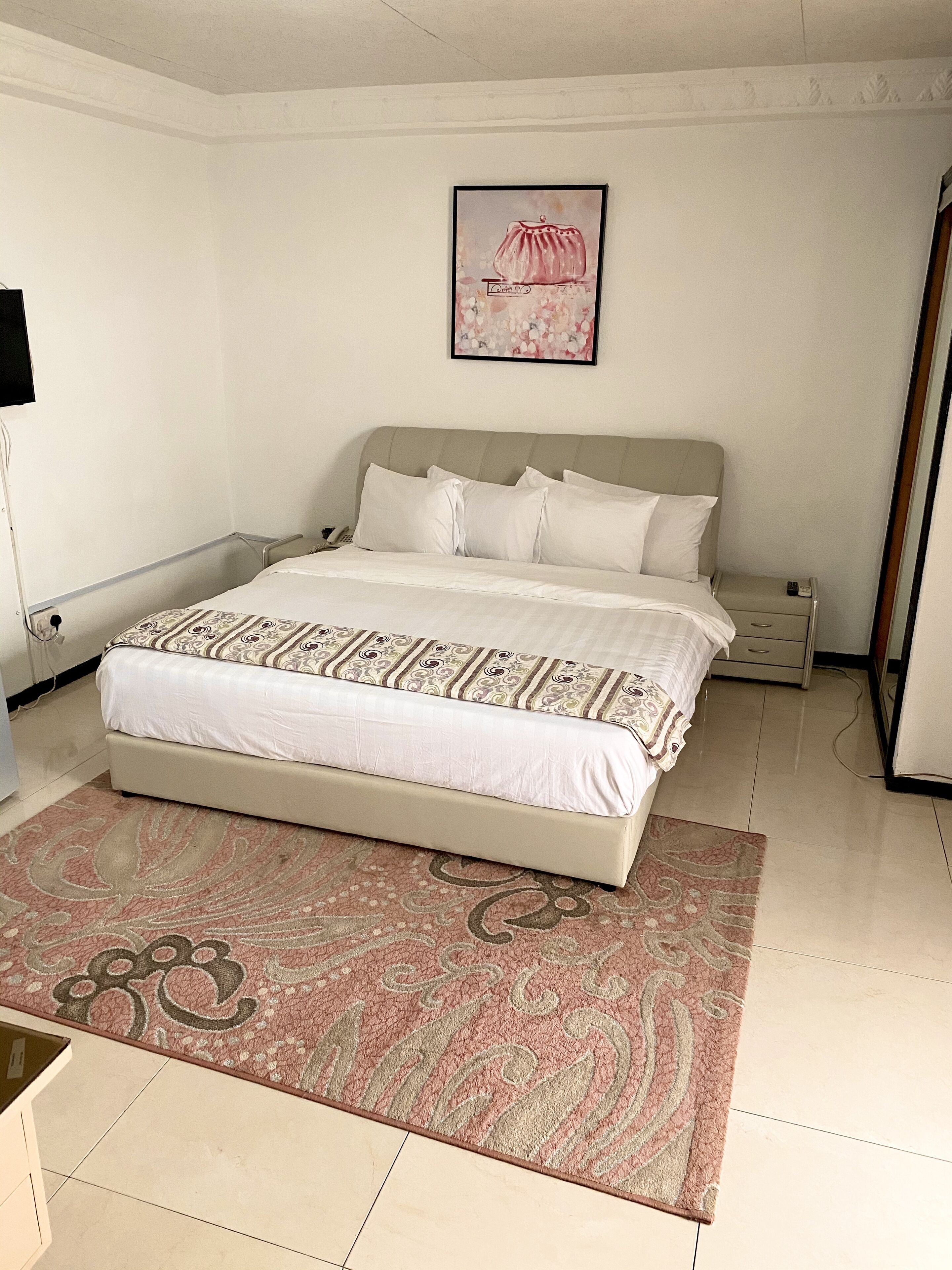 A neatly arranged bedroom with a bed, bedside tables, a nightstand, a wall-mounted TV, and a framed picture above the bed.