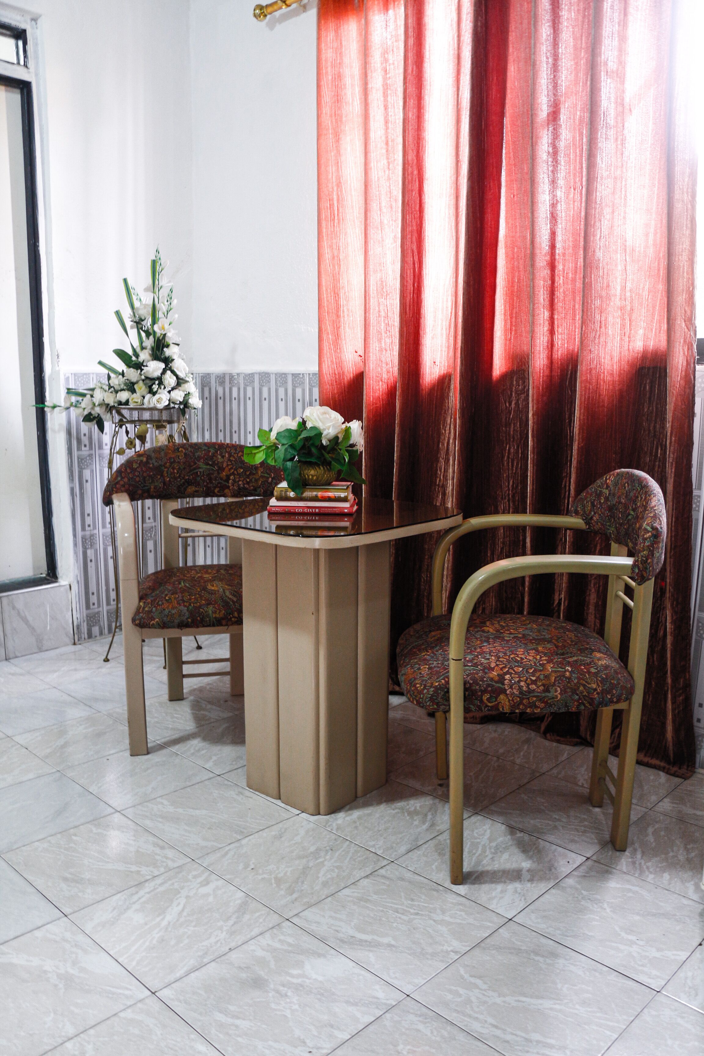 A dining area with a table and two chairs, a potted plant, and a red curtain.