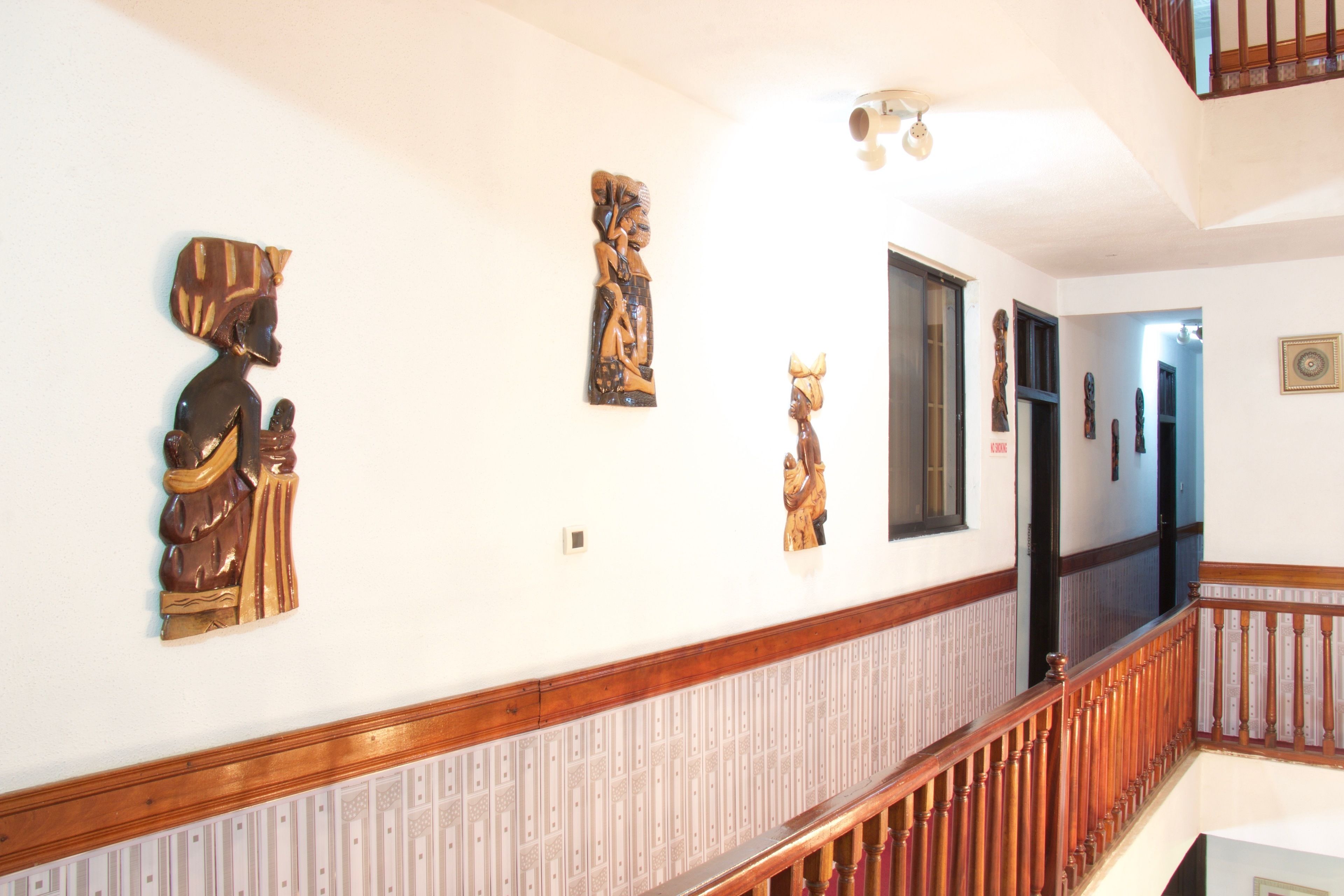 Un pasillo con barandillas de madera, un papel tapiz decorado y varias esculturas en las paredes.