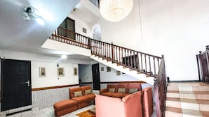 A spacious living area with a staircase, a sofa set, and a chandelier. - Hill View Hotel McCarthy Hills (Mallam)