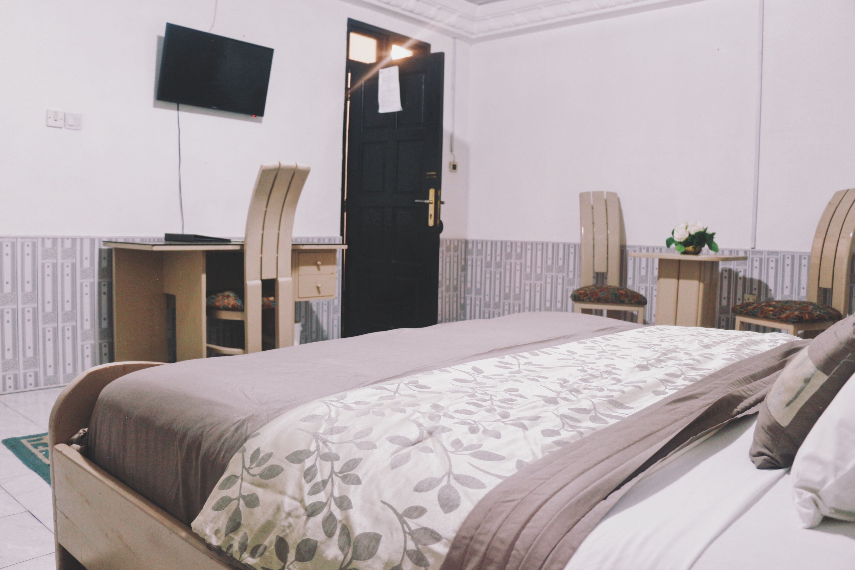 A bedroom with a bed, desk, chair, and a TV on the wall.