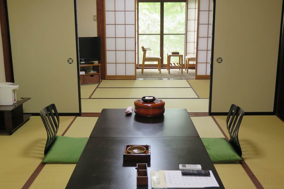 A traditional Japanese room with tatami flooring, a low table, and sliding doors leading to a garden.