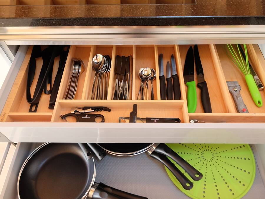 Un cajón de cocina con utensilios, una sartén y un colador.