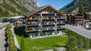 Een modern meerlaags hotel met balkons, een skilift en een berg op de achtergrond.