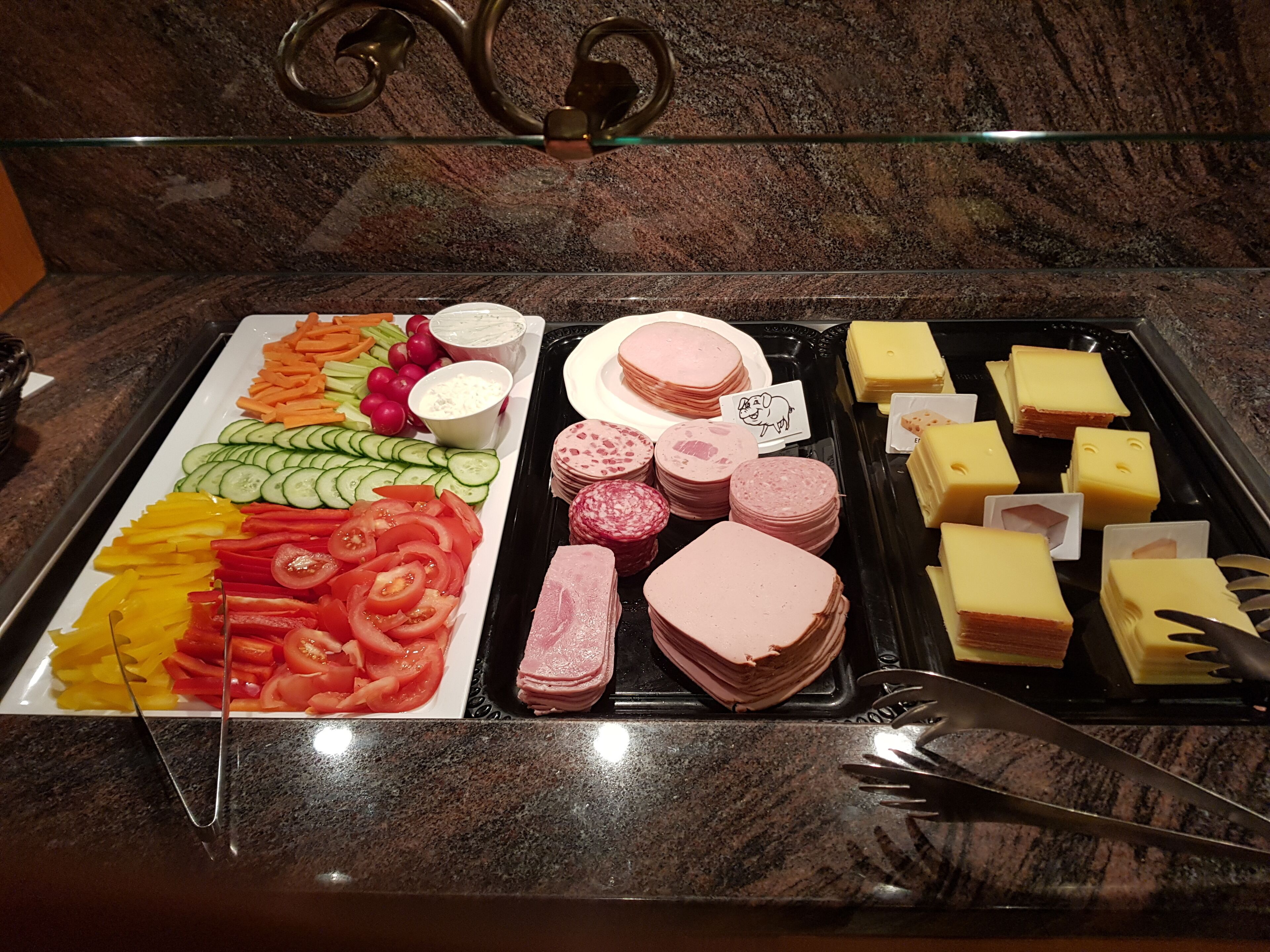 A buffet with various food items including sliced vegetables, meats, and cheeses.