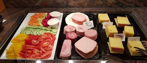 Un bufé con diversos alimentos, entre ellos verduras cortadas, carnes y quesos.