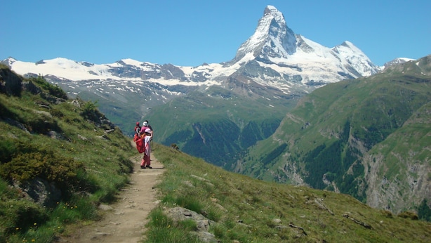 Een bergpad met wandelaars en een besneeuwde bergtop op de achtergrond.