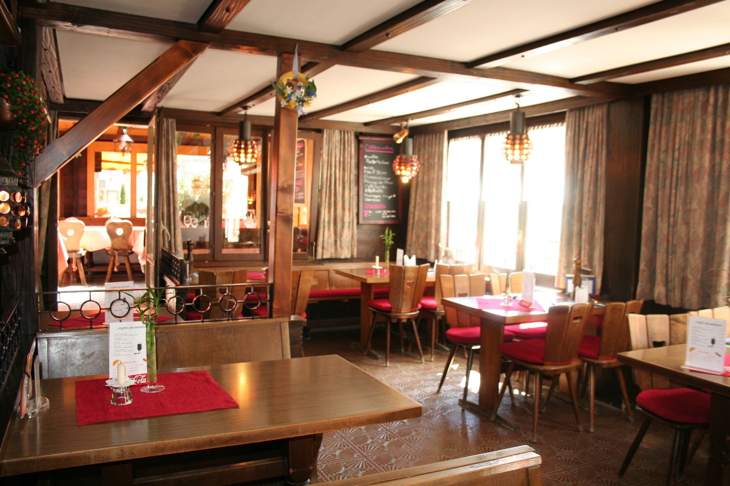 A restaurant interior with wooden tables and chairs, red cushions, and a menu board.